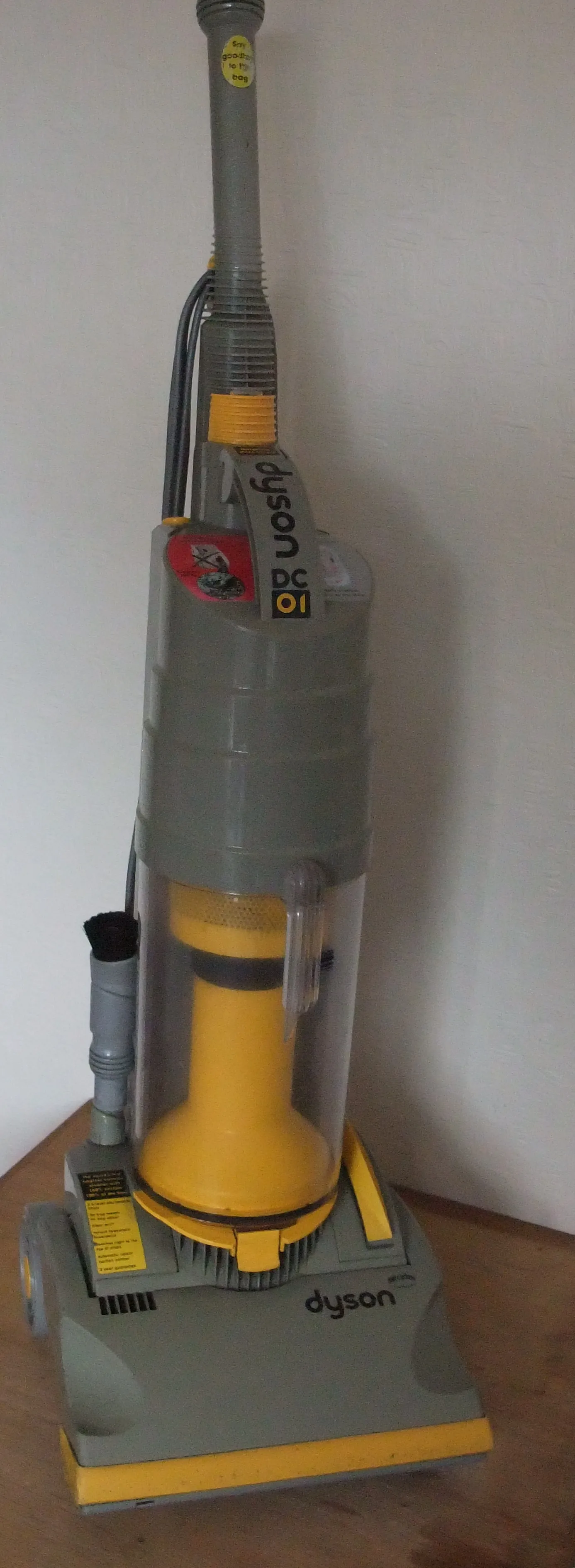 A yellow Dyson DC01 upright vacuum cleaner standing on a wooden floor