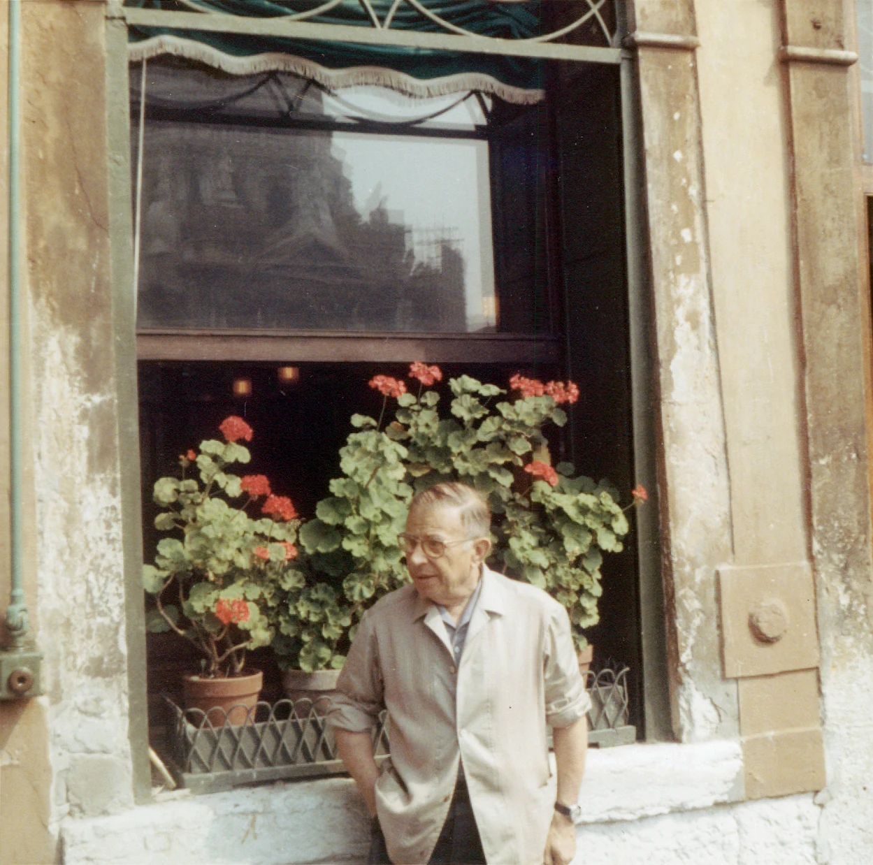 Jean-Paul Sartre standing at a cafe window with geraniums in Venice, August 1967